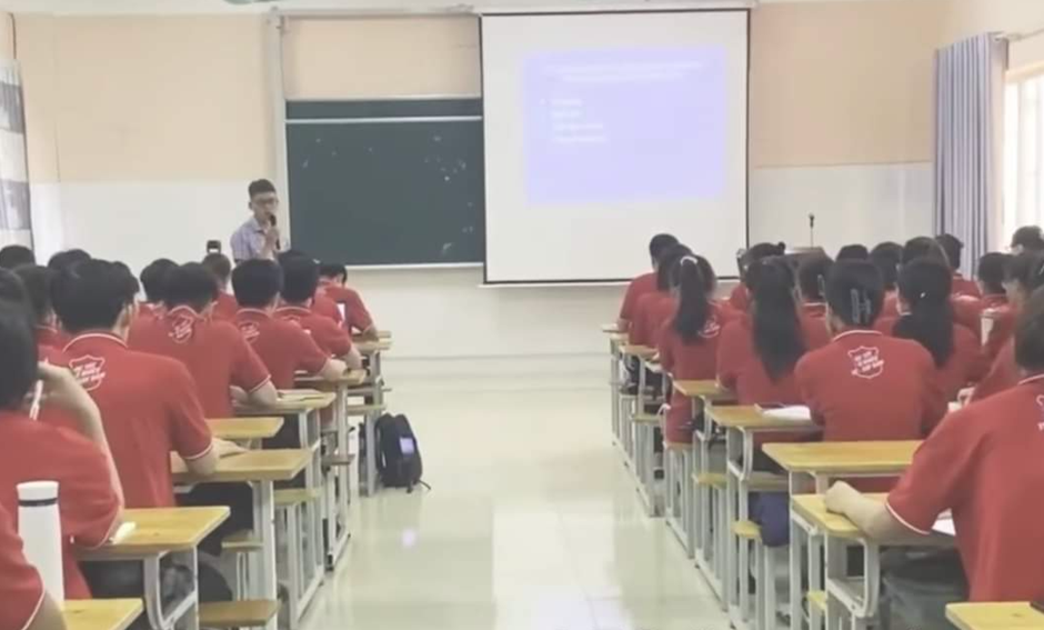 A person in a red shirt in front of a classroom

Description automatically generated